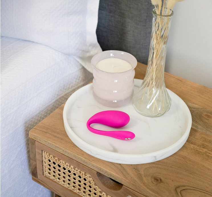 Rosa Vibro-Ei auf rundem Tablett neben Kerze und Vase auf Holzboard