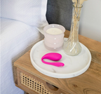 Rosa Vibro-Ei auf rundem Tablett neben Kerze und Vase auf Holzboard